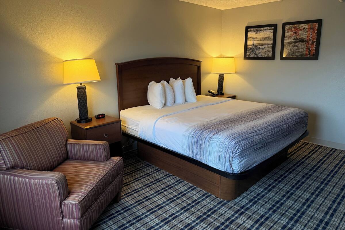 A hotel room with a bed, two bedside lamps, a chair, and two framed pictures on the wall.