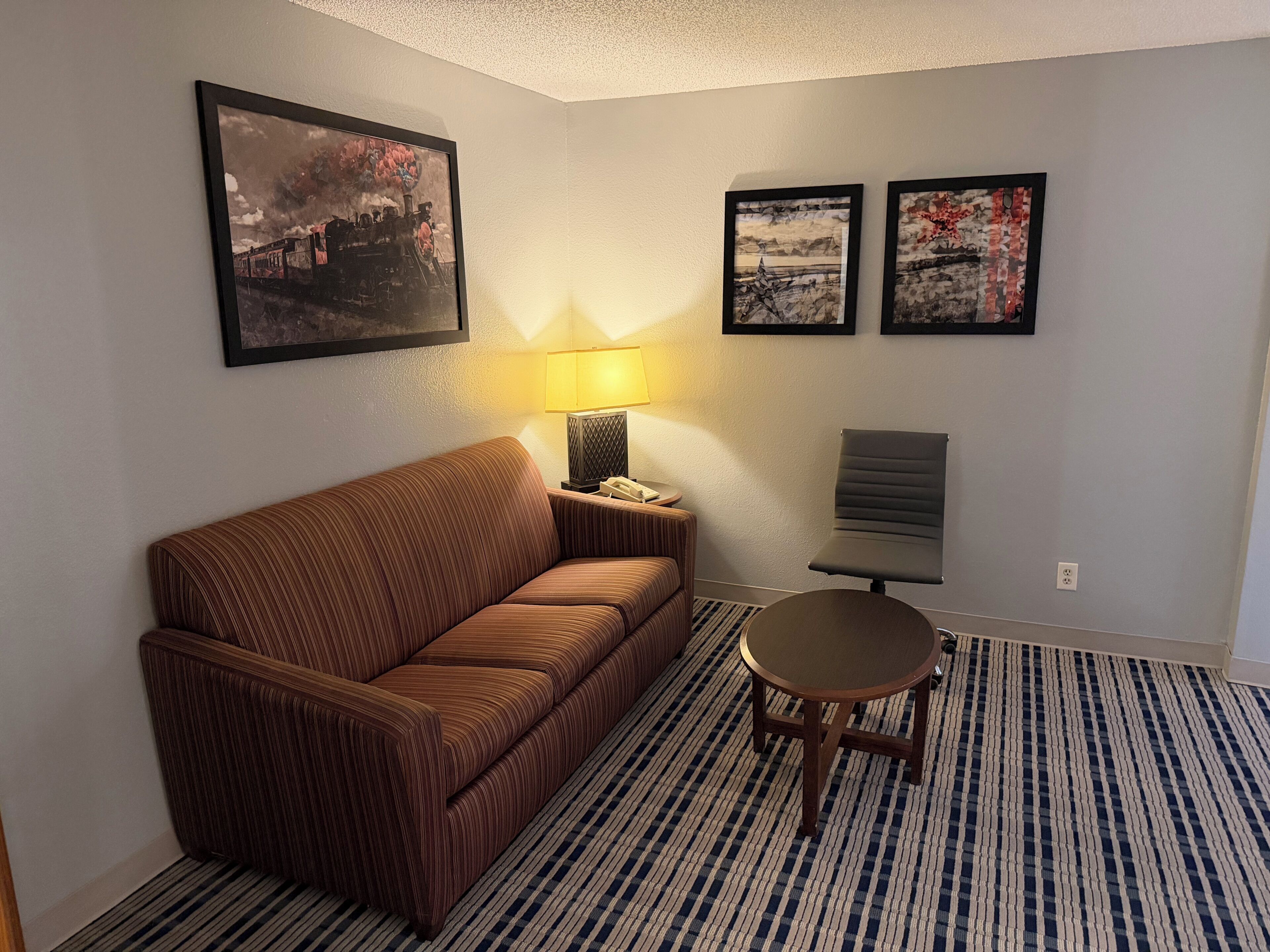 A hotel room with a striped sofa, a round table, and three framed pictures on the wall.