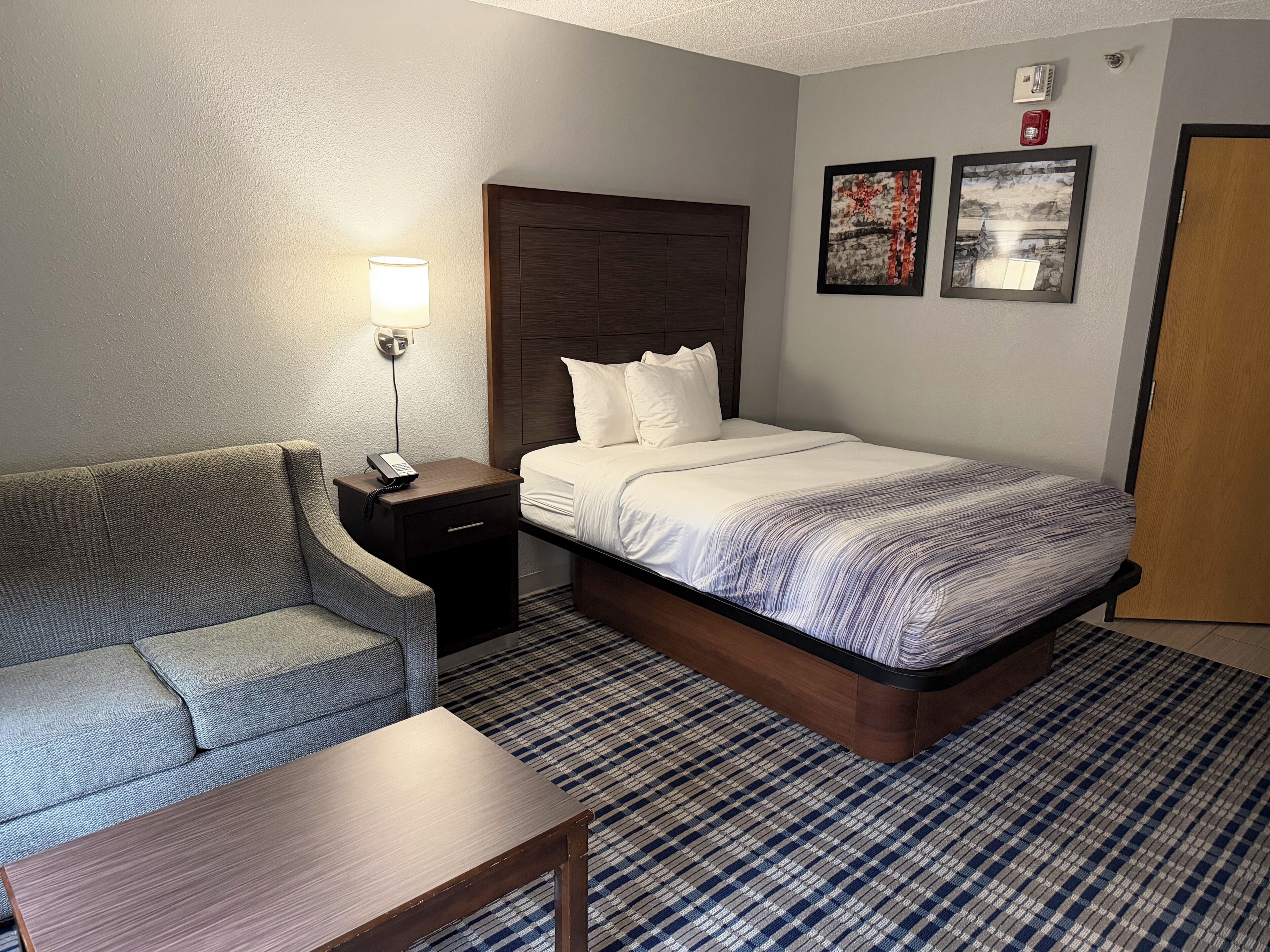 A hotel room with a bed, a nightstand with a lamp, a sofa, and a small table.