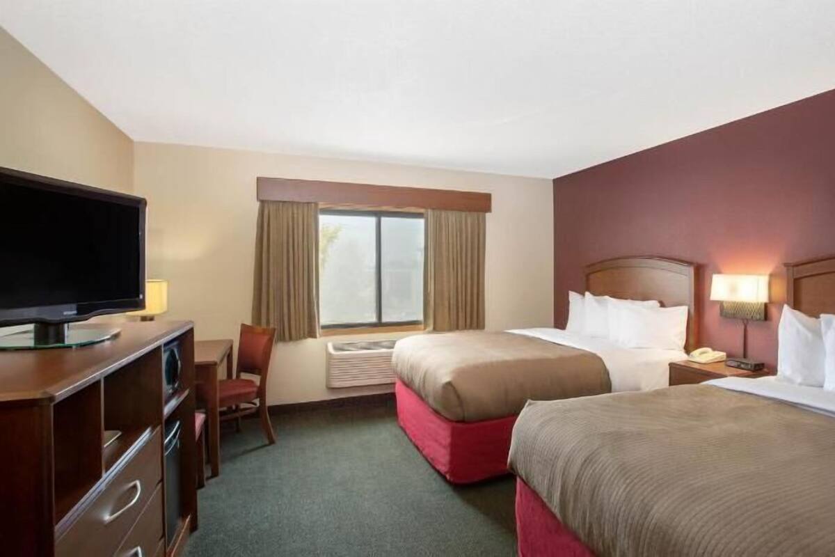 A hotel room with two beds, a TV, a desk, and a chair.