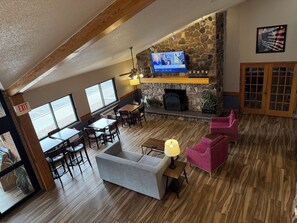 A spacious room with a stone fireplace, wooden flooring, a television mounted on the wall, and a seating area with a sofa and chairs. - AmericInn by Wyndham Kearney (Kearney)