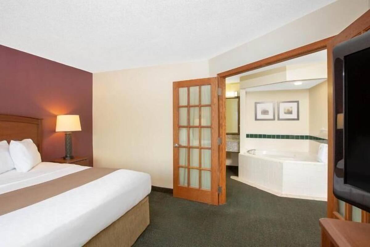 A hotel room with a bed, a desk with a lamp, a television, and a bathroom with a bathtub.