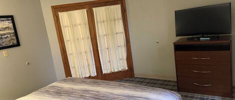 A hotel room with a bed, a television on a wooden dresser, and a door with curtains.