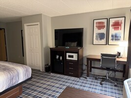 Una habitación de hotel con cama, televisión, escritorio con silla y microondas.