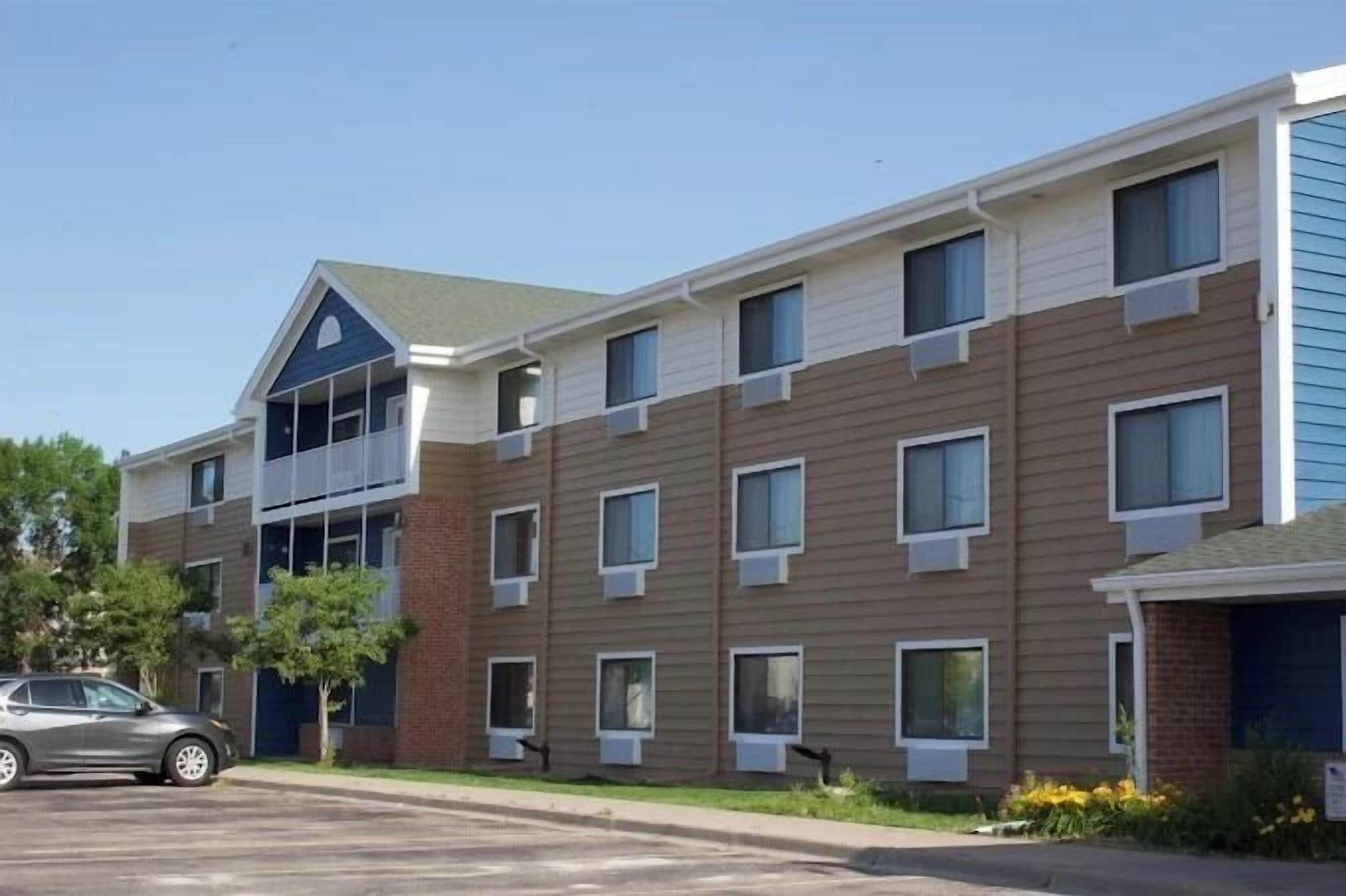 A multi-story residential building with a flat roof, multiple windows, and a car parked in front.
