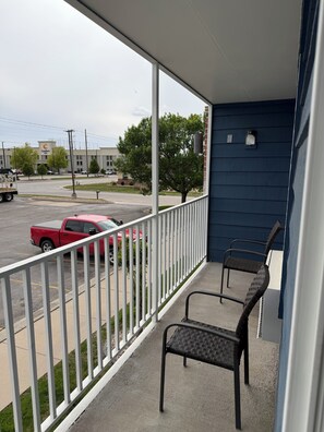 Un balcón con barandal blanco, dos sillas y vista a una calle con un camión rojo y un edificio Comfort Inn.