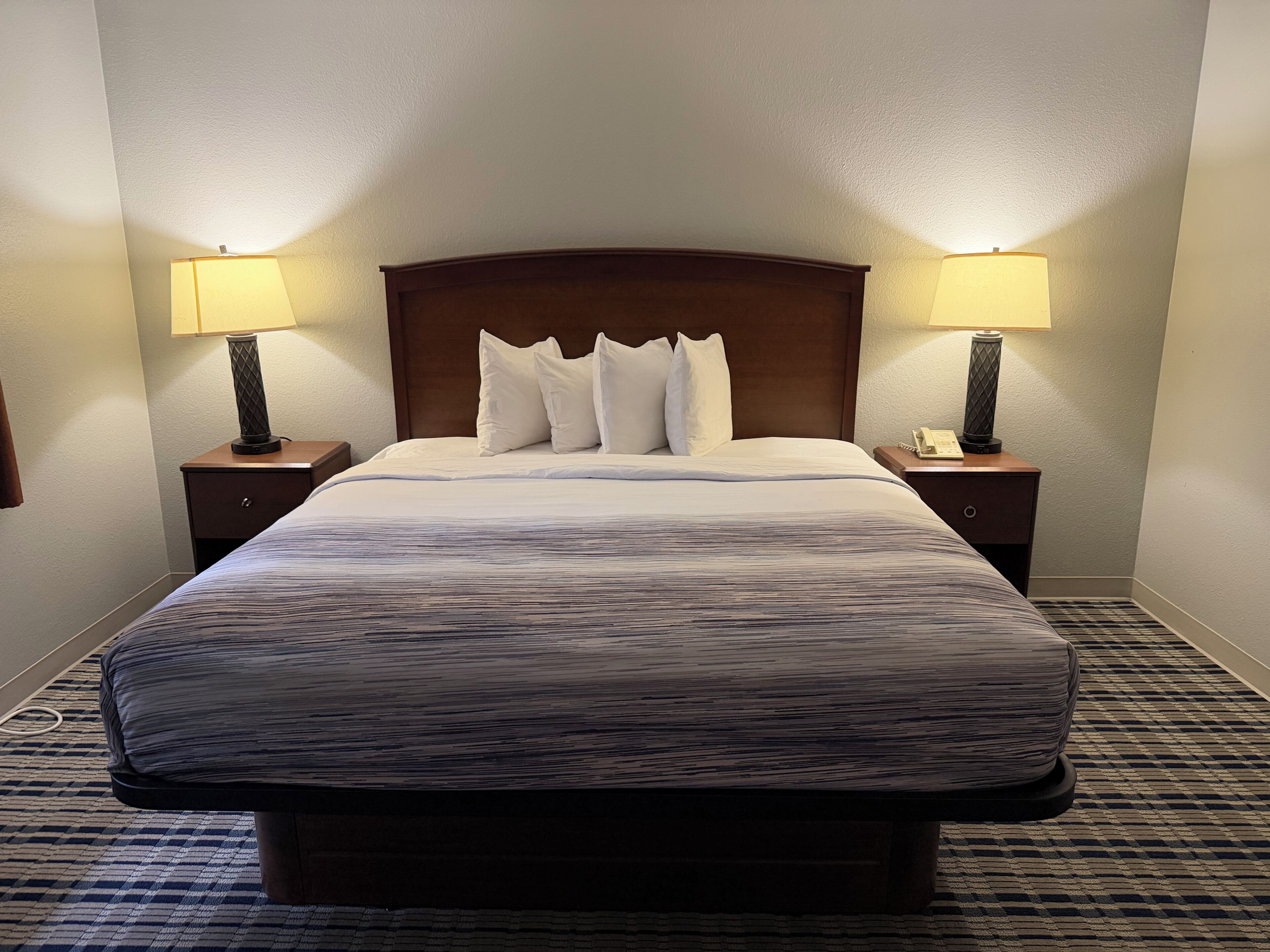 A hotel room with a large bed, two bedside tables with lamps, and a patterned carpet.