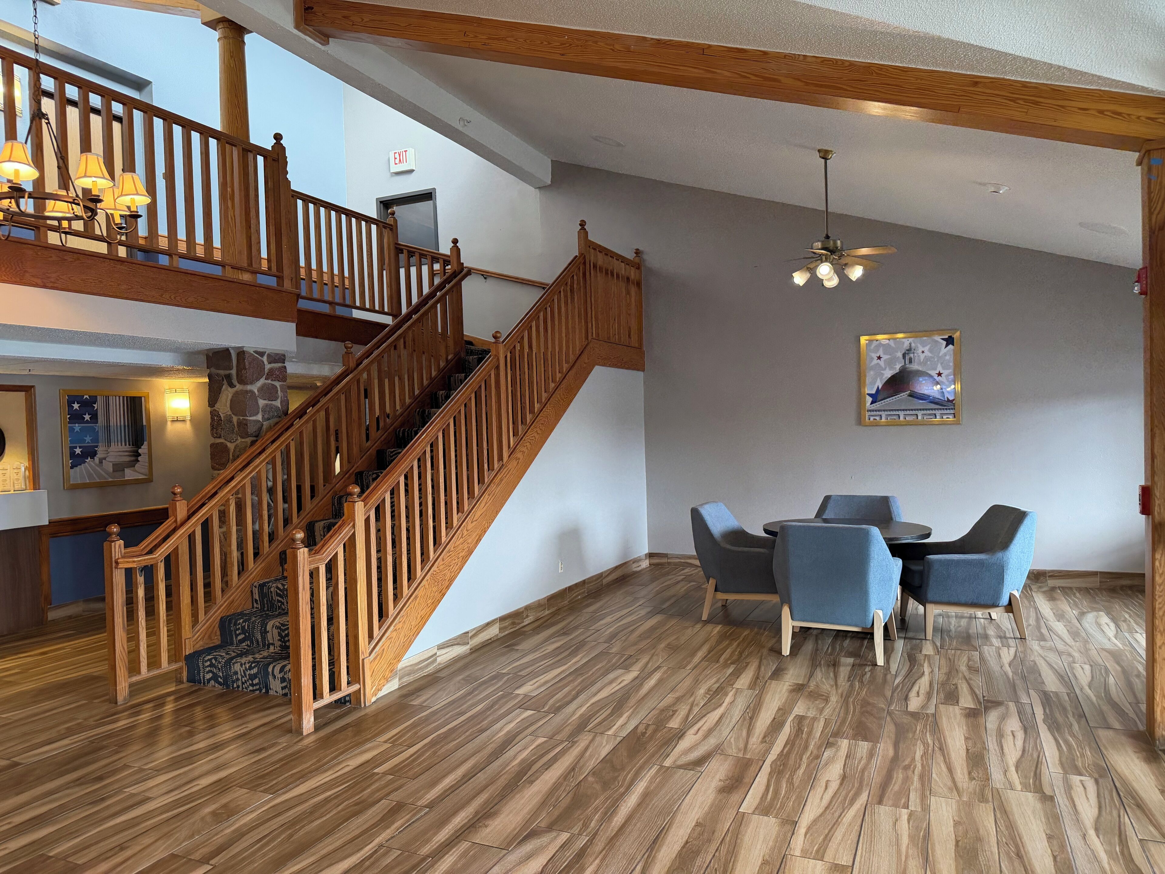A spacious lobby with a wooden staircase, a dining area with blue chairs, and a ceiling fan.