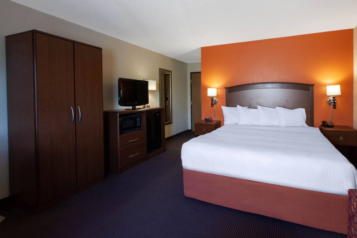 A hotel room with a large bed, a TV, a wardrobe, and two bedside lamps.