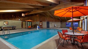 Una piscina interior con techo de madera, sombrillas naranjas y una mesa de billar.