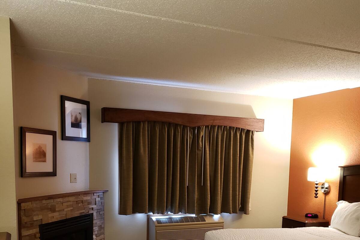 A hotel room with a fireplace, a bed, a nightstand, and a wall-mounted lamp.