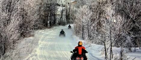 A snowy road with a person riding a snowmobile.