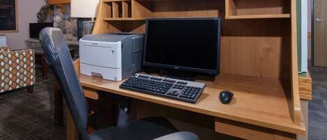 A home office setup with a wooden desk, a computer monitor, a keyboard, a mouse, and a printer.