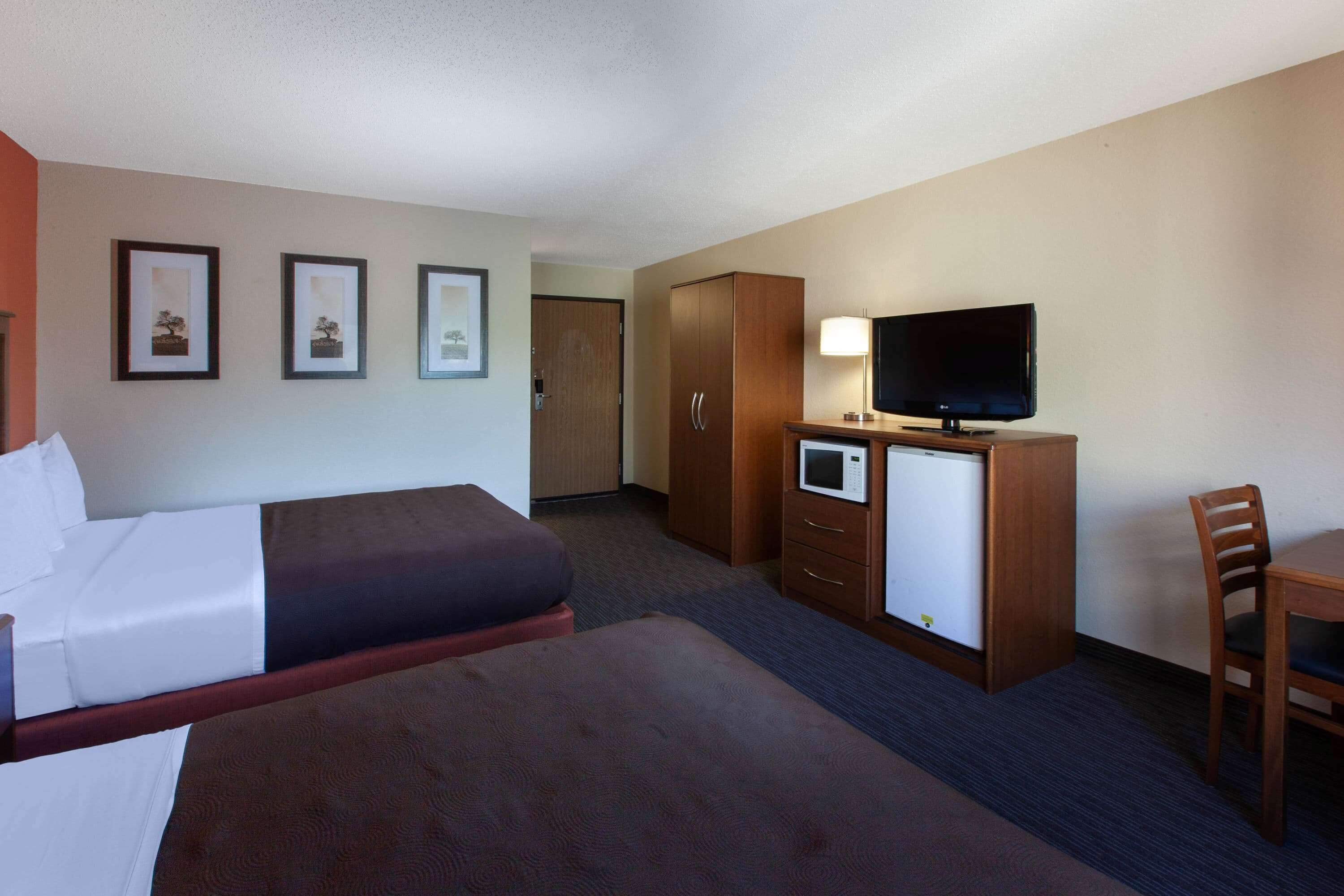 A hotel room with two beds, a desk with a television, a microwave, and a wardrobe.