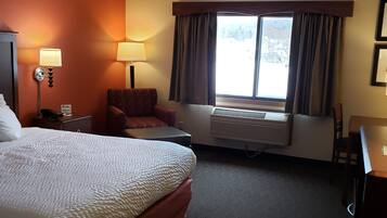A hotel room with a large bed, a desk, a chair, a lamp, and a window with curtains.