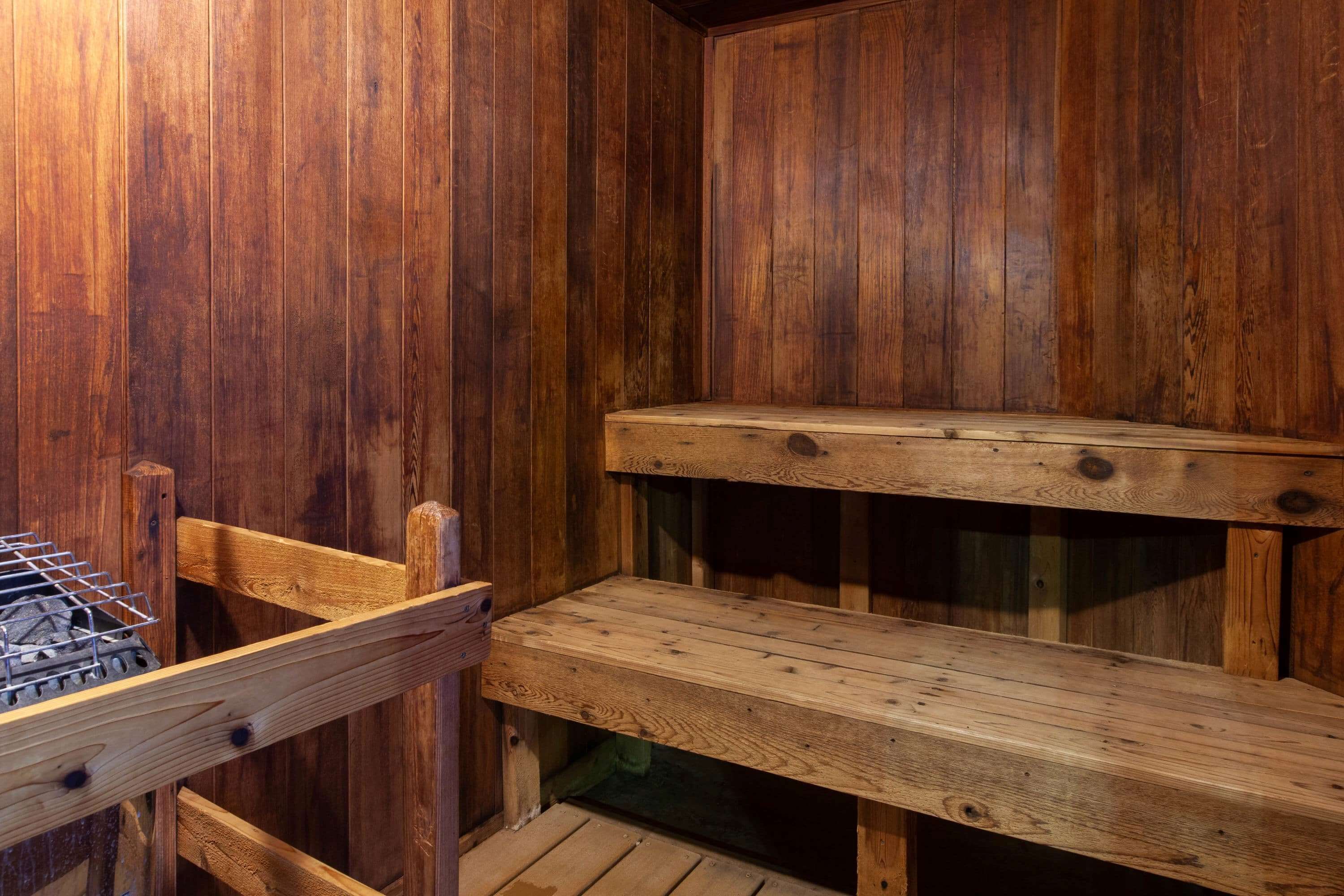 A wooden sauna with benches and a metal grill.