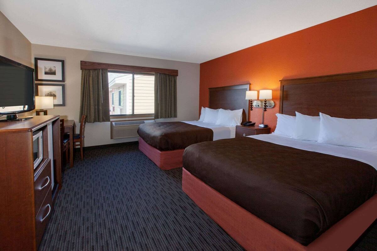 A hotel room with two beds, a TV, a desk with a chair, and a window with curtains.