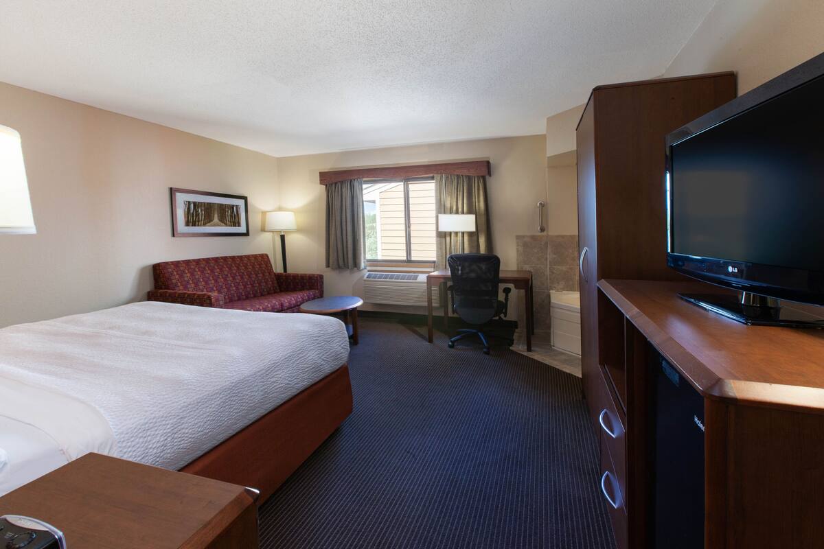 A hotel room with a large bed, a desk with a chair, a television, and a window with curtains.