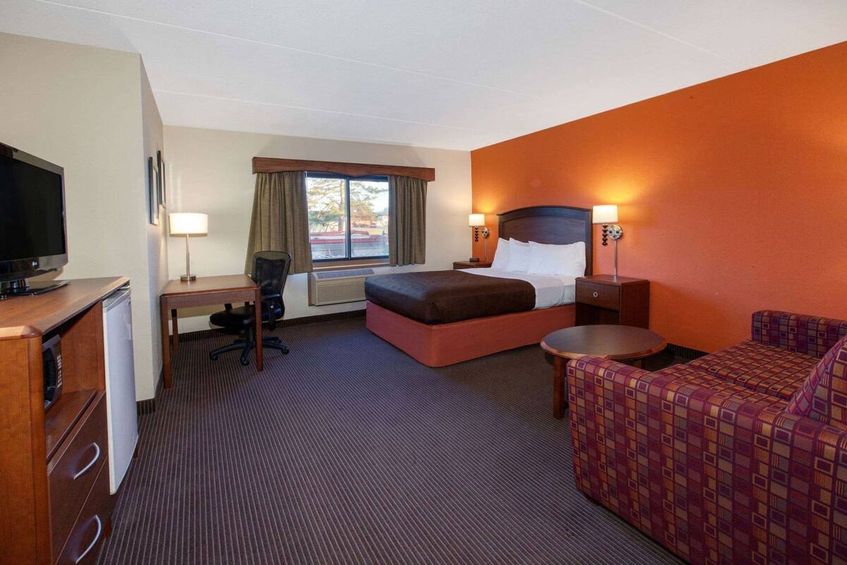A hotel room with a bed, desk, chair, television, and a small table.