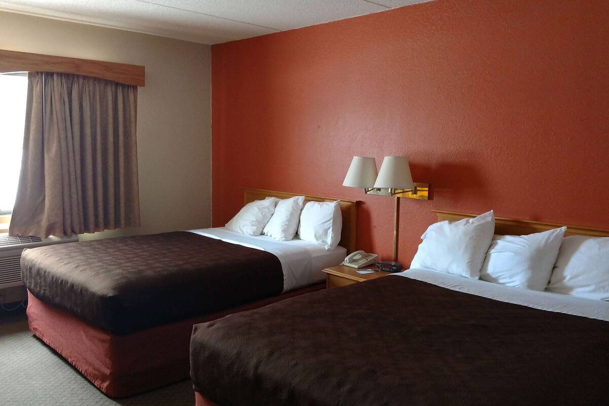 A hotel room with two beds, a nightstand with a lamp, and a window with curtains.