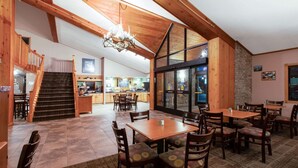 Un comedor amplio con mesas y sillas de madera, una escalera que lleva a un nivel superior y una cocina al fondo.