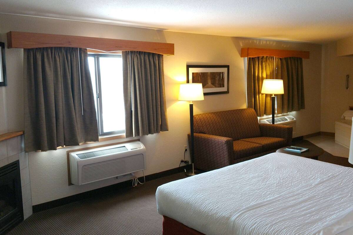 A hotel room with a large bed, a chair, a desk, and a window with curtains.