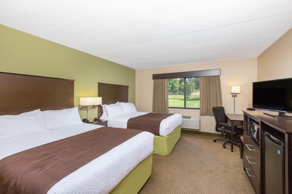 A hotel room with two beds, a desk, a TV, and a view of the outdoors.