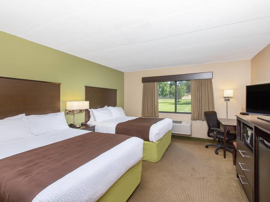 A hotel room with two beds, a desk, a TV, and a view of the outdoors.
