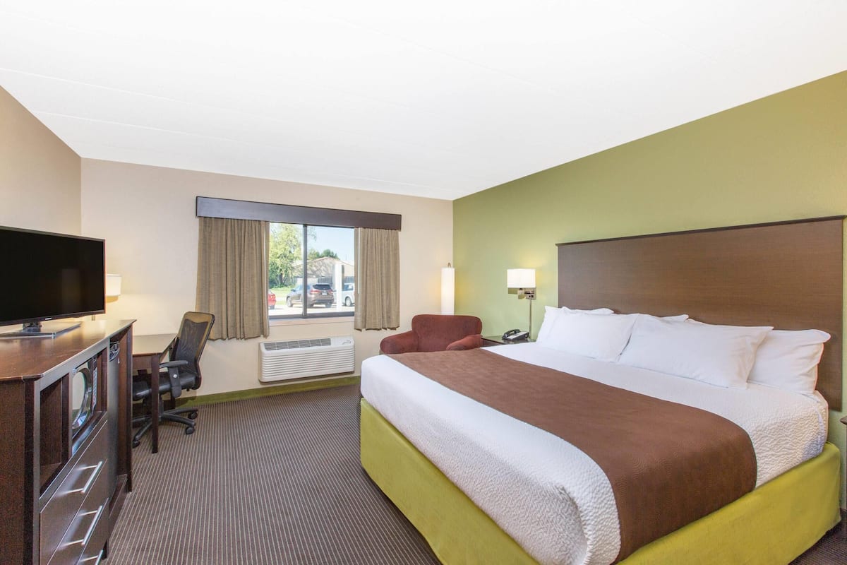 A hotel room with a bed, a desk with a TV, a chair, a window with curtains, and a lamp.
