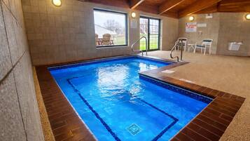 An indoor swimming pool with tiled walls, a wooden ceiling, and a view of a grassy area outside.