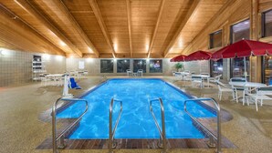 An indoor swimming pool with wooden ceiling beams, tiled walls, and white furniture.