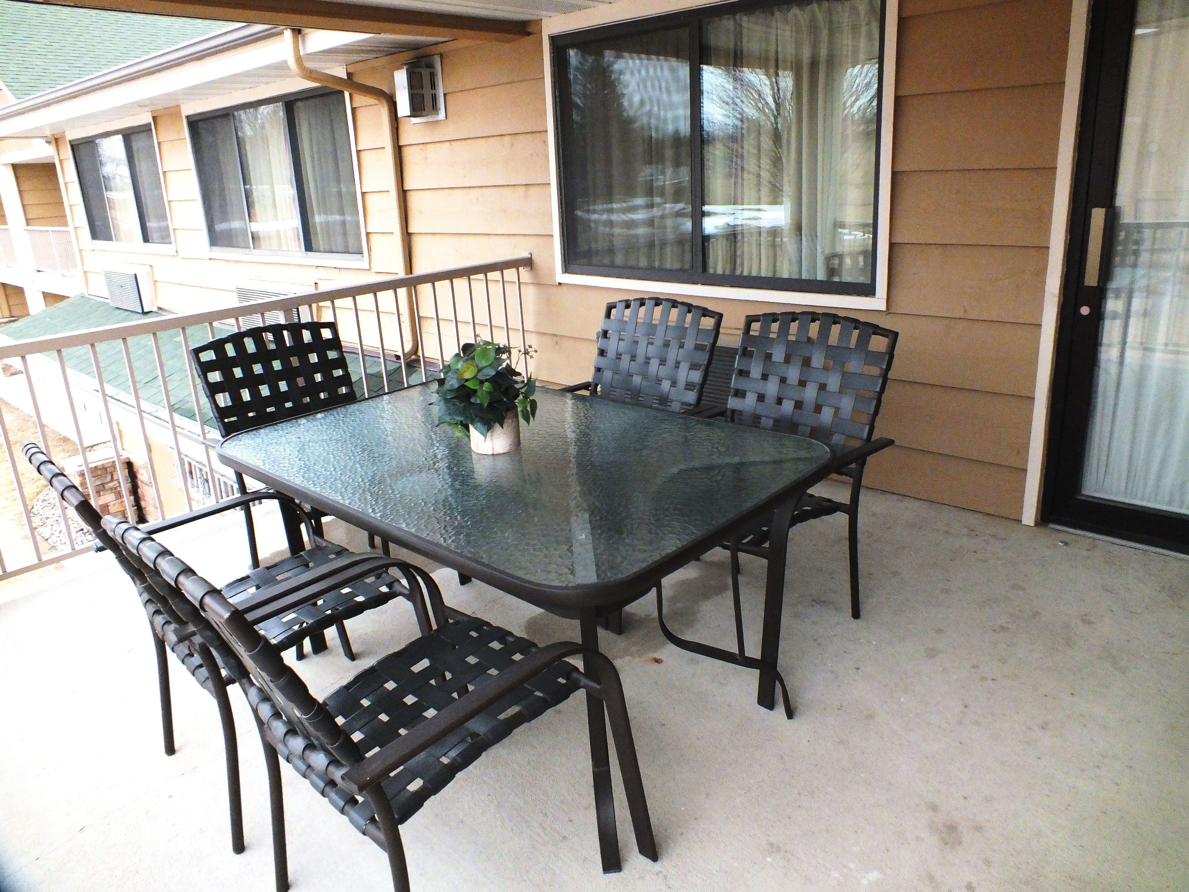 A glass-top table with four chairs, a potted plant, and a window with curtains.
