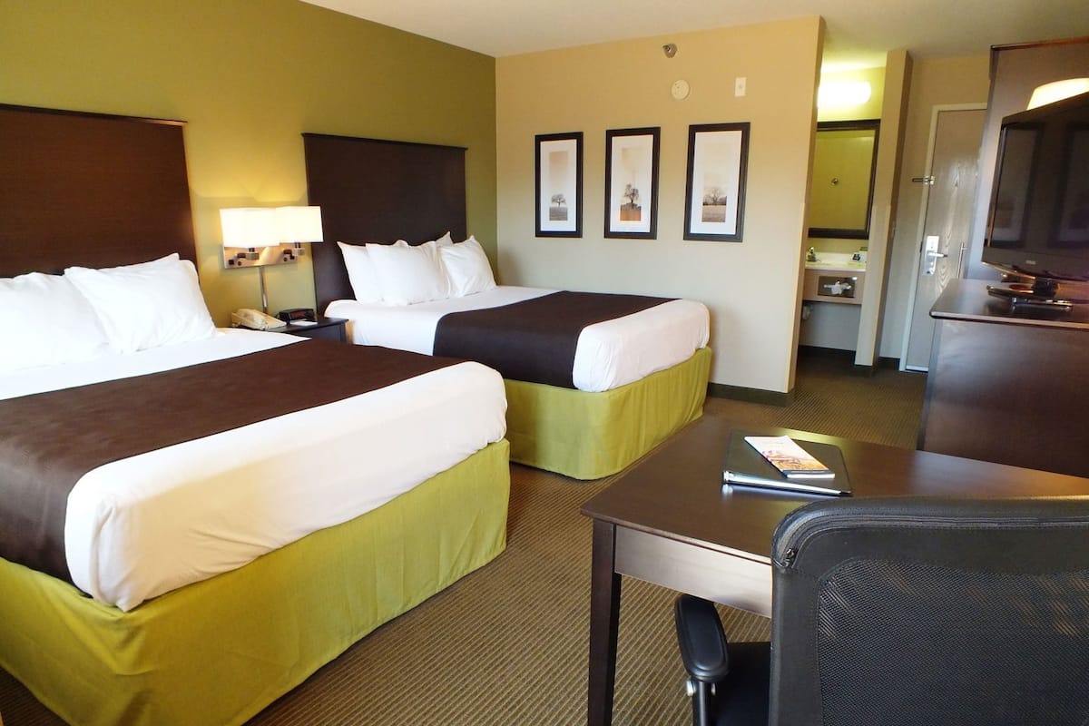 A hotel room with two beds, a desk, a chair, a TV, and a bathroom visible through an open door.