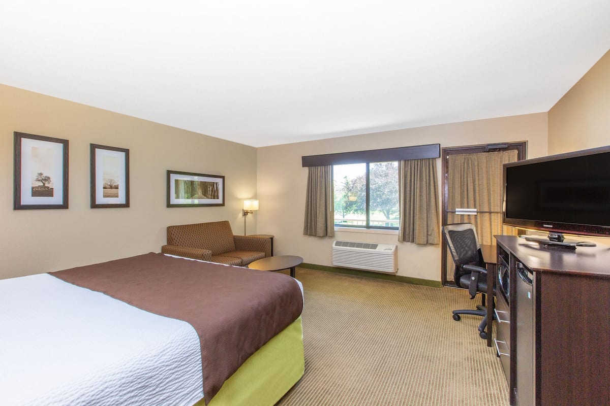 A hotel room with a bed, a desk, a chair, a television, and framed pictures on the wall.
