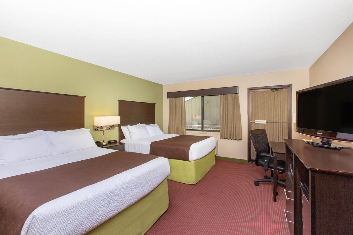 A hotel room with two beds, a desk with a TV, and a chair.