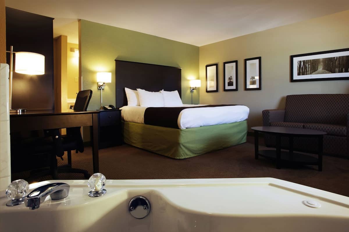 A hotel room with a bed, a desk, a chair, a sofa, a bathtub, and framed pictures on the wall.