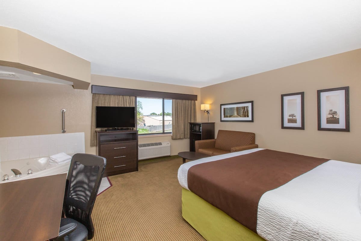 A hotel room with a bed, a desk with a computer, a chair, a TV, and a window.