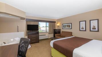 A hotel room with a bed, a desk with a computer, a chair, a TV, and a window.
