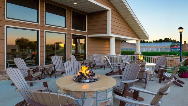 An outdoor patio with Adirondack chairs, a stone fire pit, and a view of a hotel in the background.