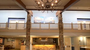 A hotel lobby with a chandelier, a reception desk, and a balcony with railings.