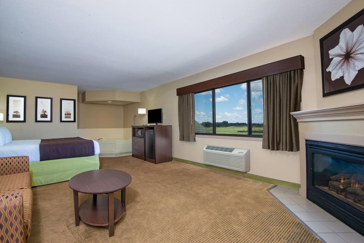 A hotel room with a bed, a sofa, a small table, a fireplace, a television, a desk, and a large window with a view.