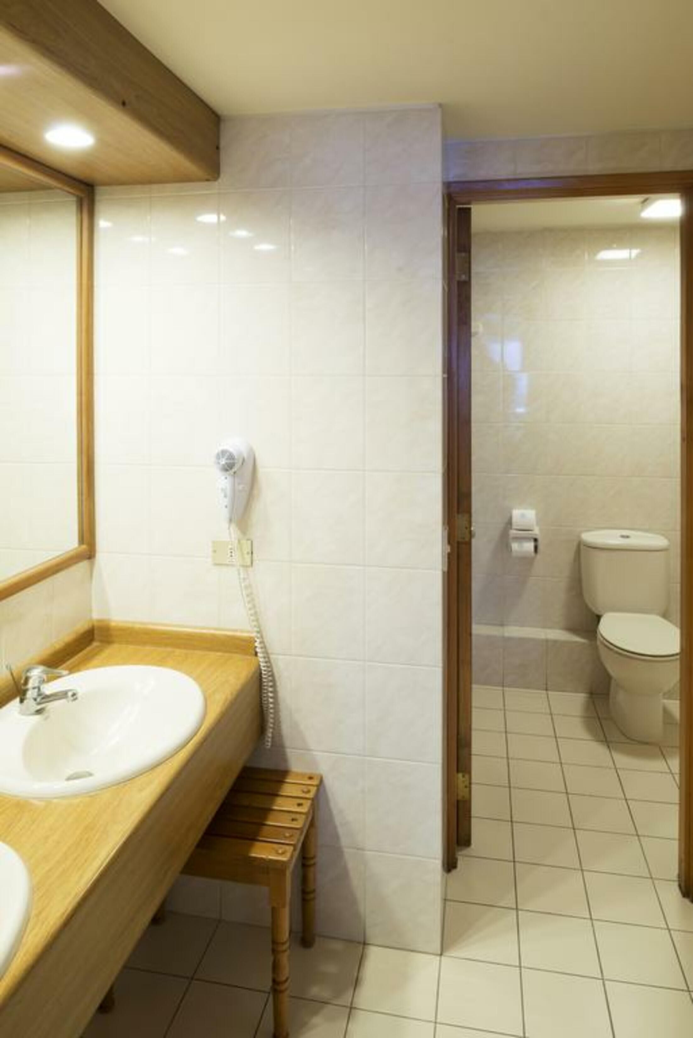 Ein Badezimmer mit einem Holzkosmetikschrank, einem weißen Waschbecken, einem Föhn und einer Toilette.