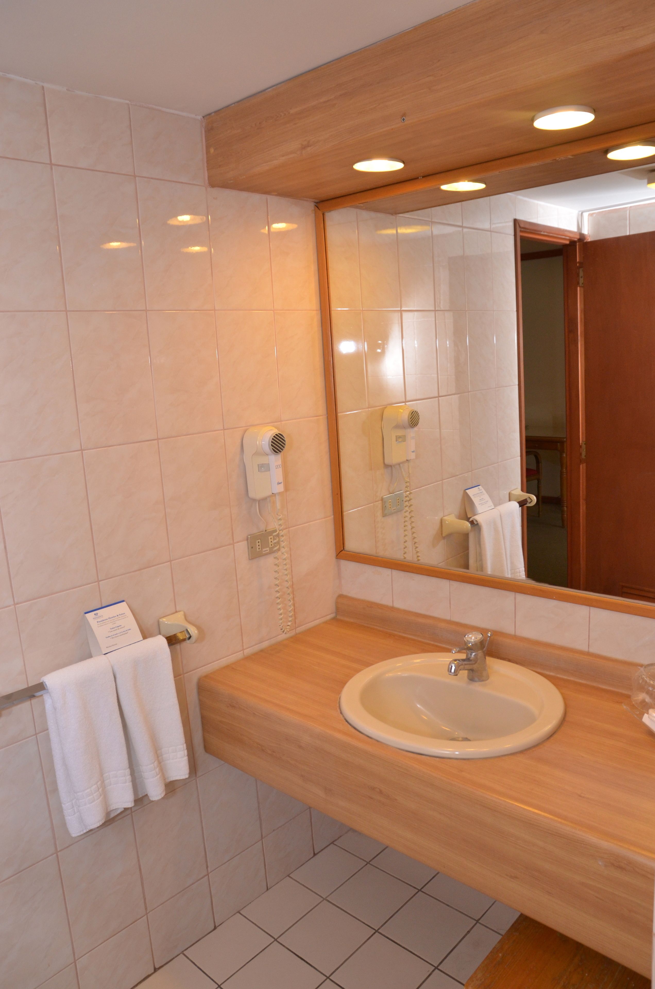 Une salle de bain avec un meuble-lavabo en bois, un évier, un miroir et un sèche-cheveux fixé au mur.