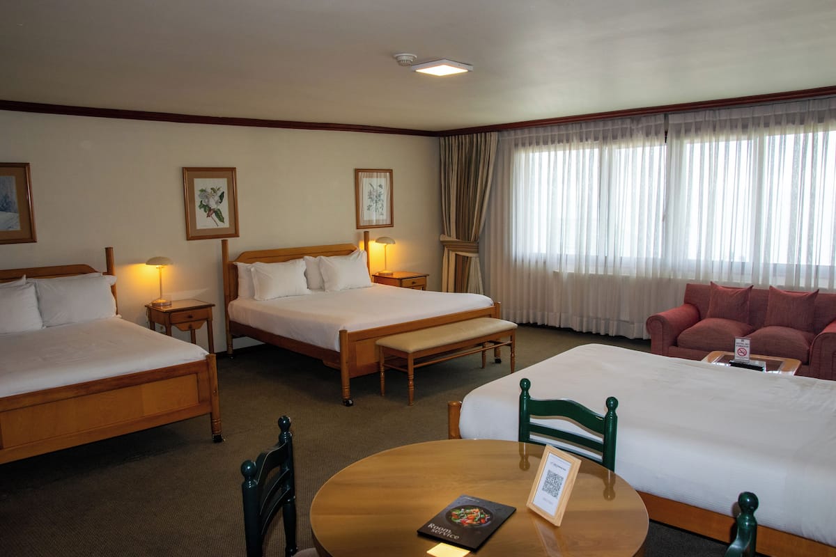 A hotel room with two beds, a sofa, a dining table, and a small desk.