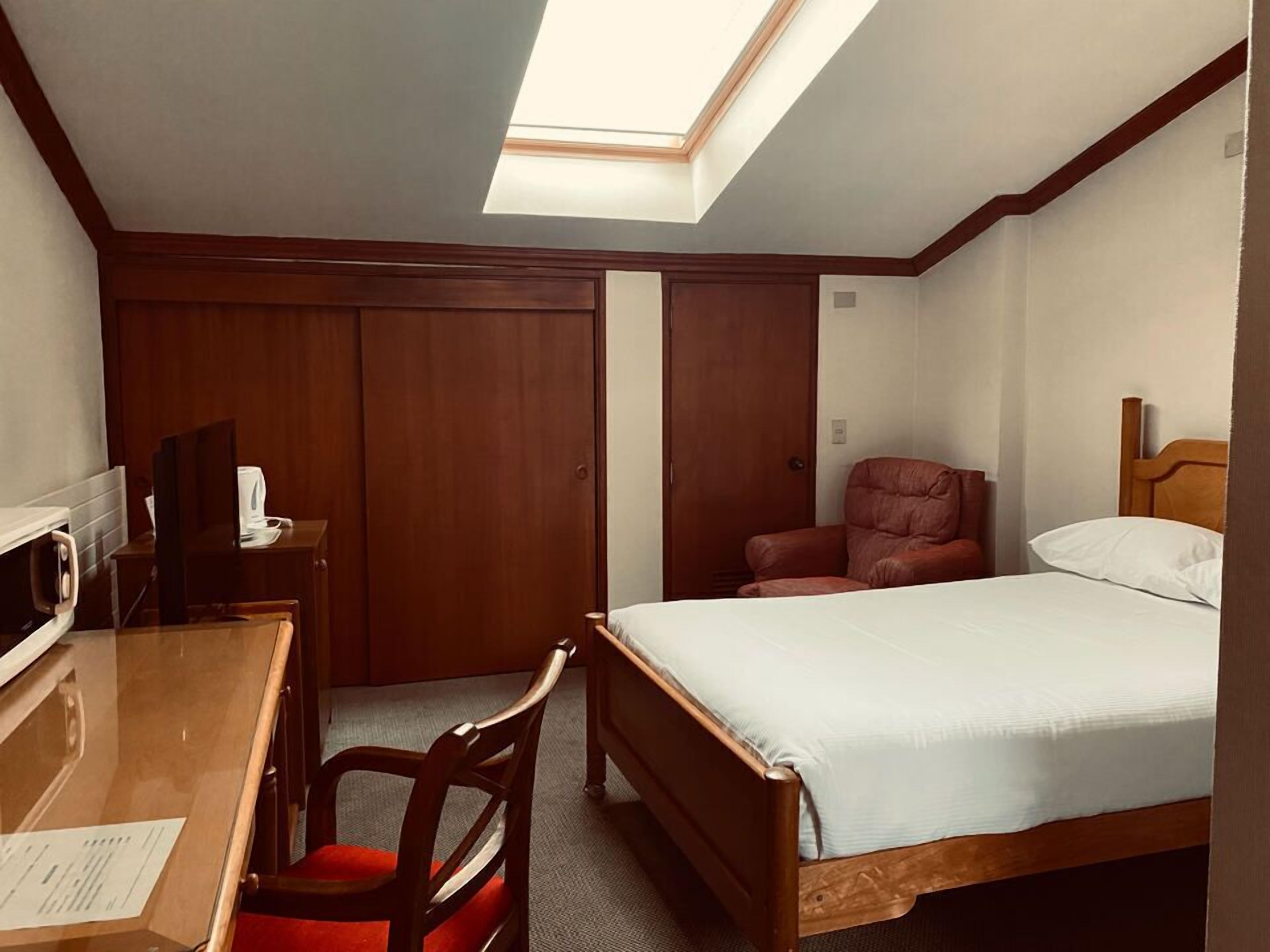 Una habitación de hotel con cama, escritorio, silla, televisor y armario.