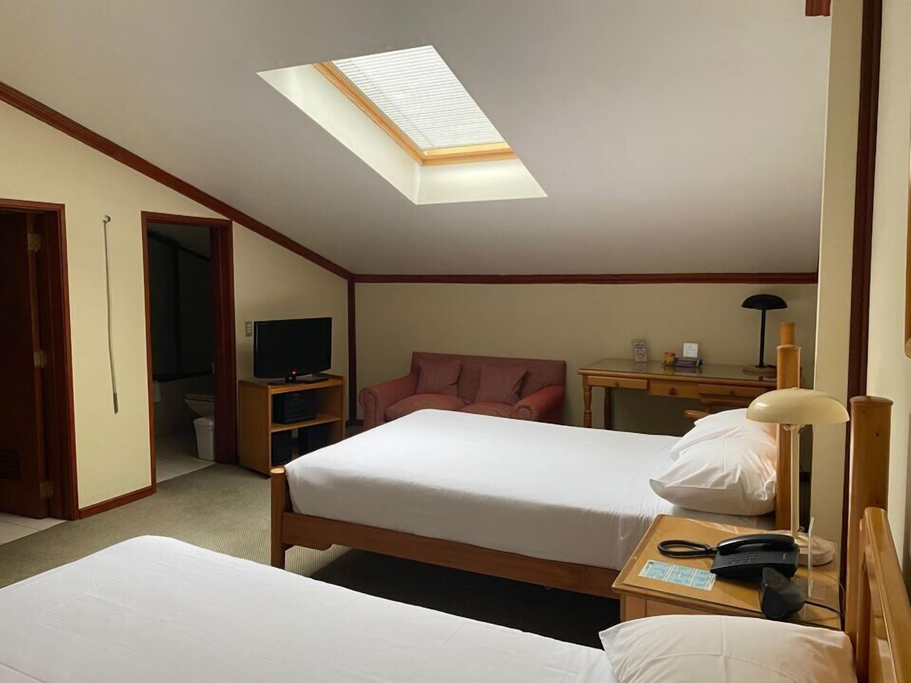 Habitación de hotel con dos camas, un escritorio, una silla, televisión y un tragaluz.
