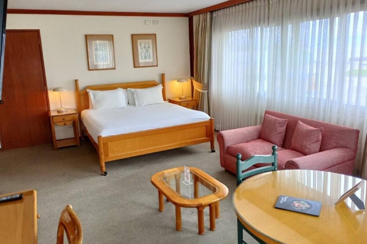 A hotel room with a bed, a sofa, a small table, and a chair.