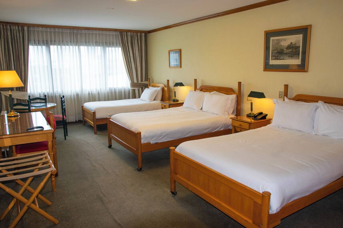 A hotel room with two single beds, a desk with a chair, a small table, and a lamp.