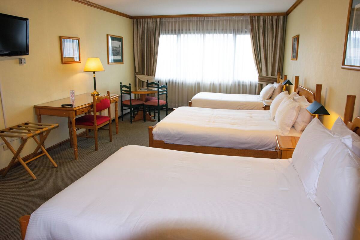 A hotel room with two beds, a desk, a chair, a TV, and a window with curtains.