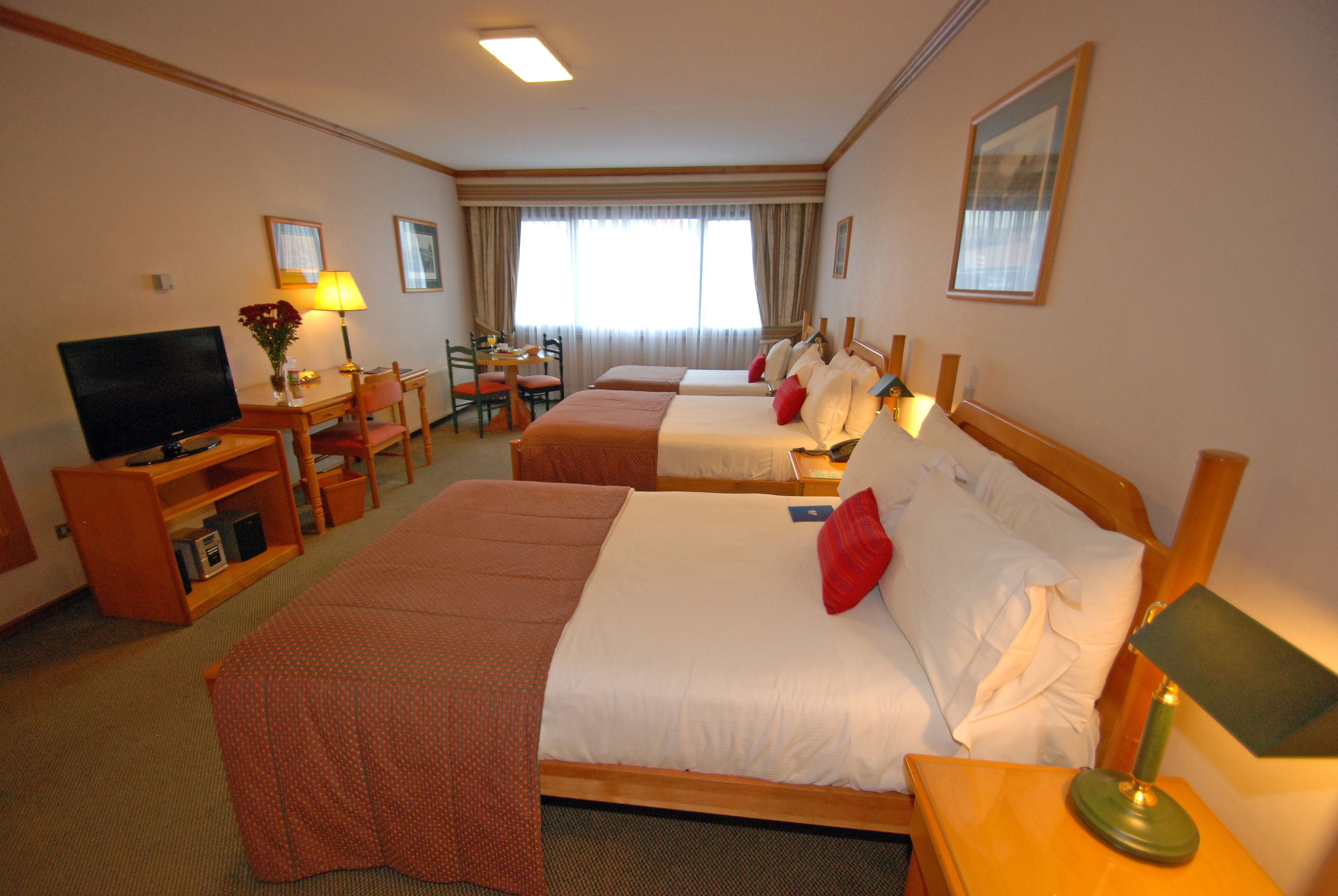 Ein Hotelzimmer mit zwei Betten, einem Schreibtisch, einem Stuhl, einem Fernseher und einer Lampe.